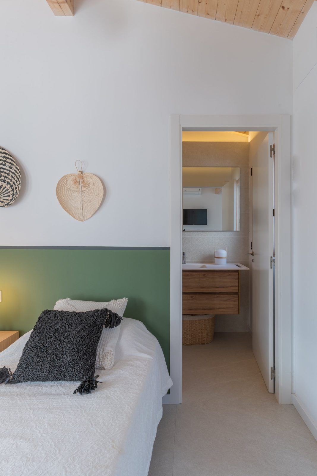 Bedroom with a green painted headboard band, woven wall fans and an en-suite bathroom