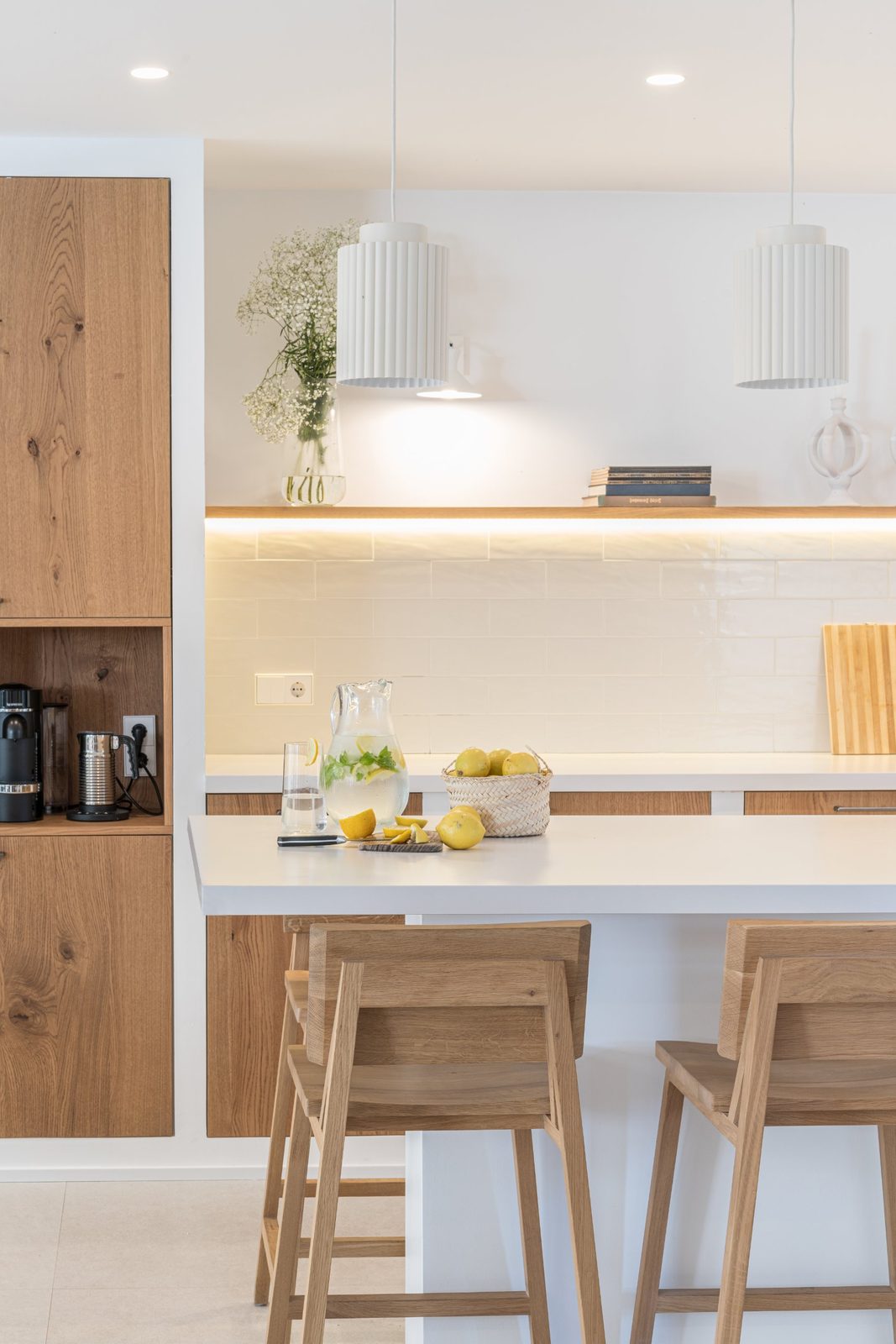 Kitchen island styled with lemons beneath white fluted pendants and a backlit oak shelf
