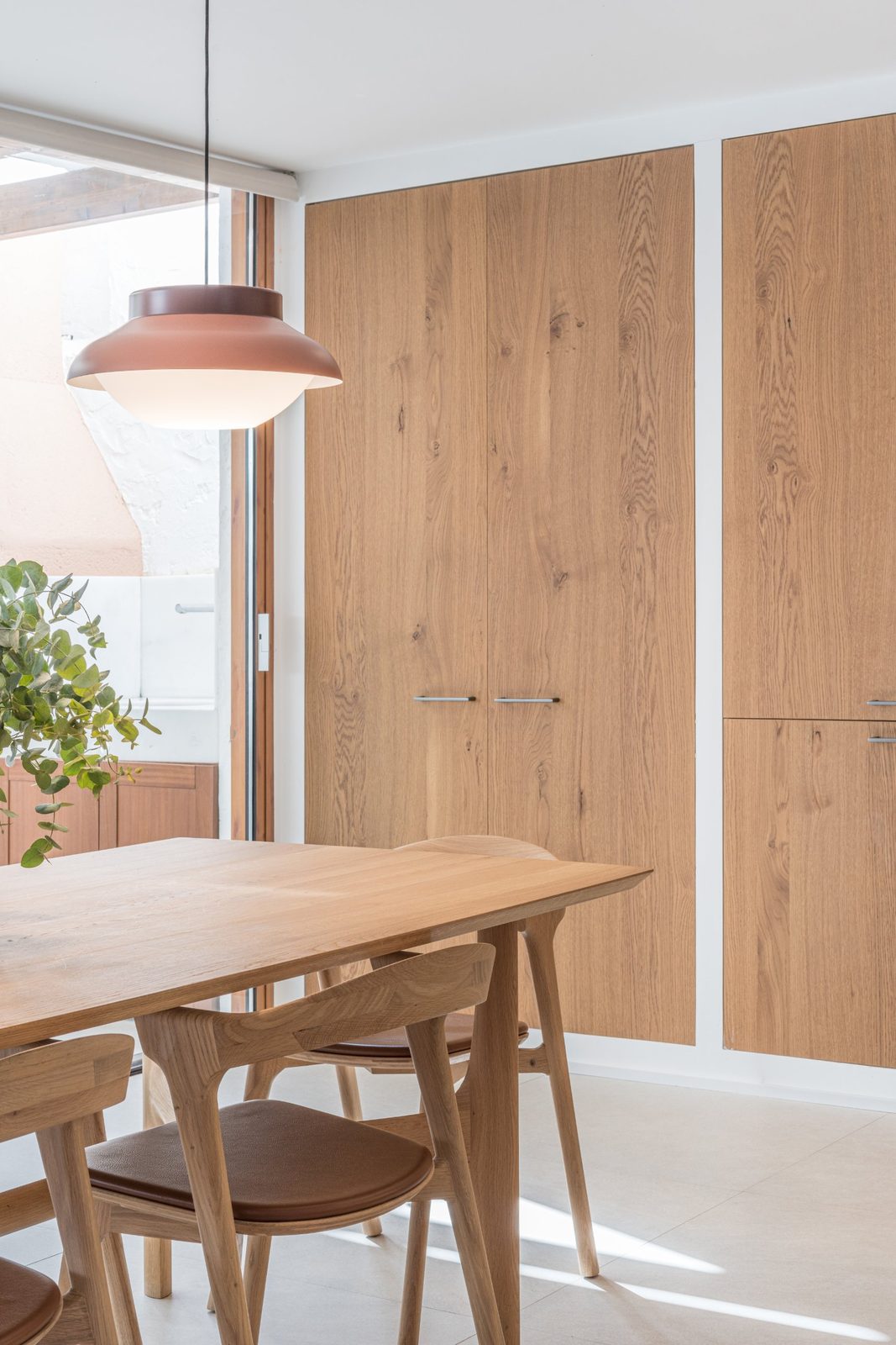 Oak dining table and chairs under a terracotta pendant, with built-in oak cabinets
