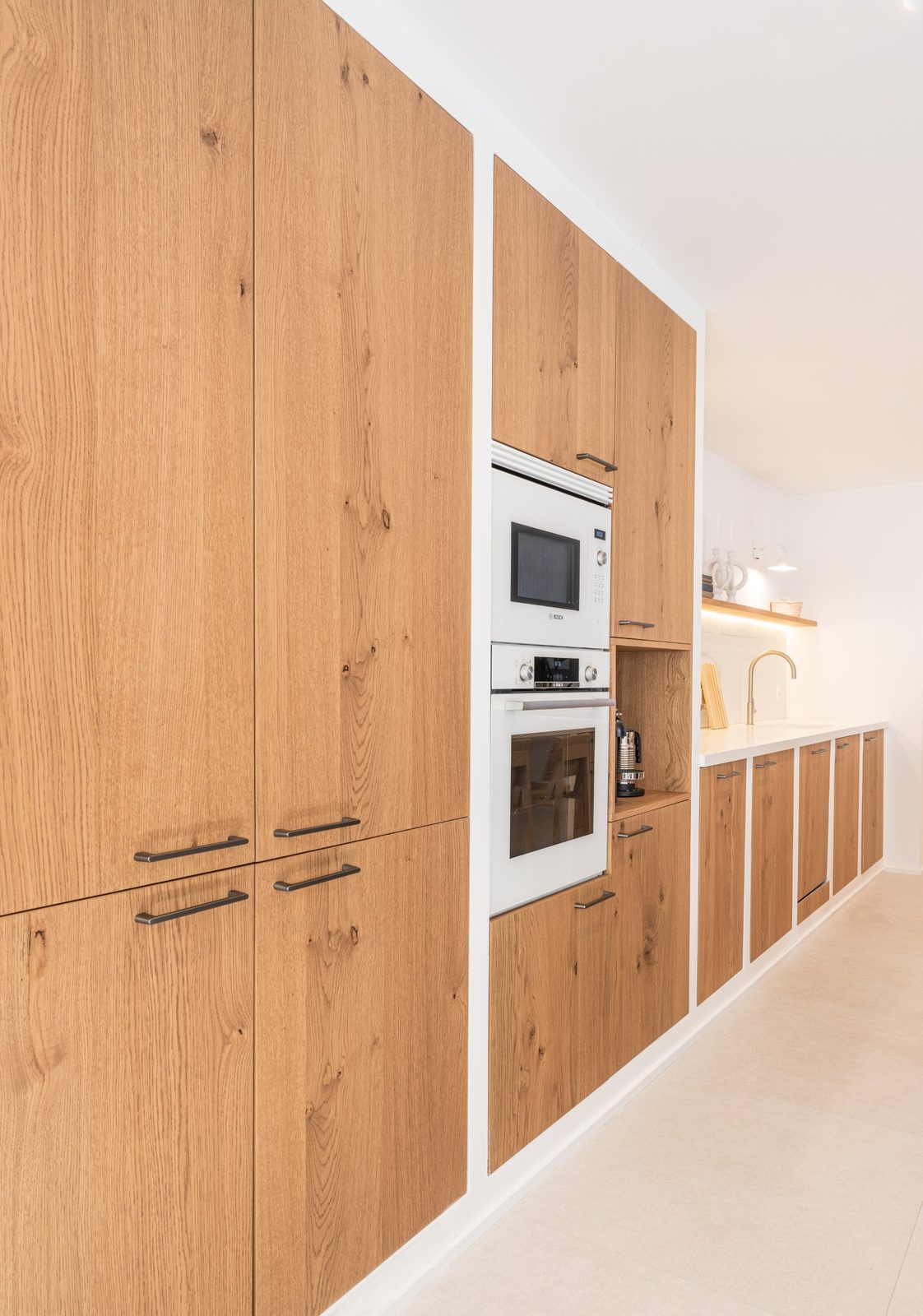 Wall of knotty oak kitchen cabinets with white built-in ovens and a coffee niche