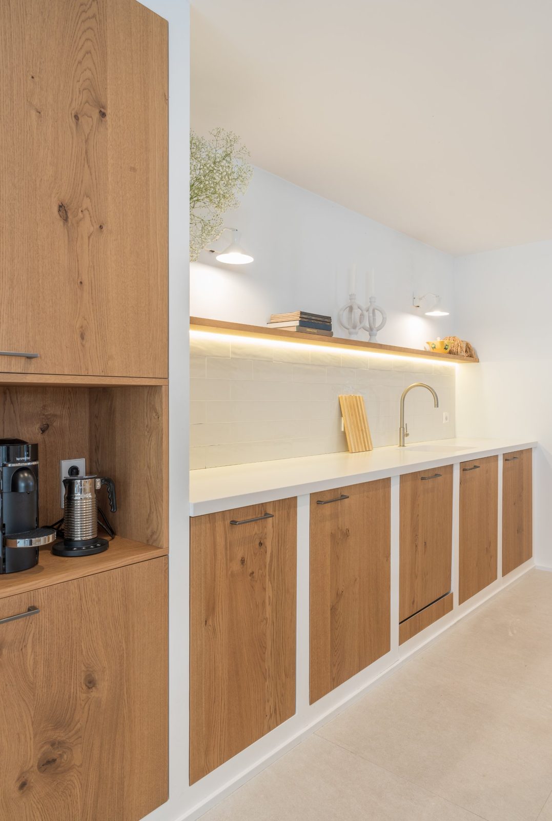 Run of oak base units with white zellige-style splashback, brass tap and lit shelf