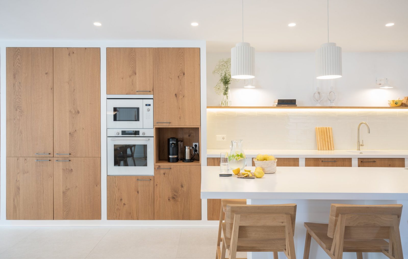 Symmetrical oak kitchen wall with built-in ovens, open shelf and white island