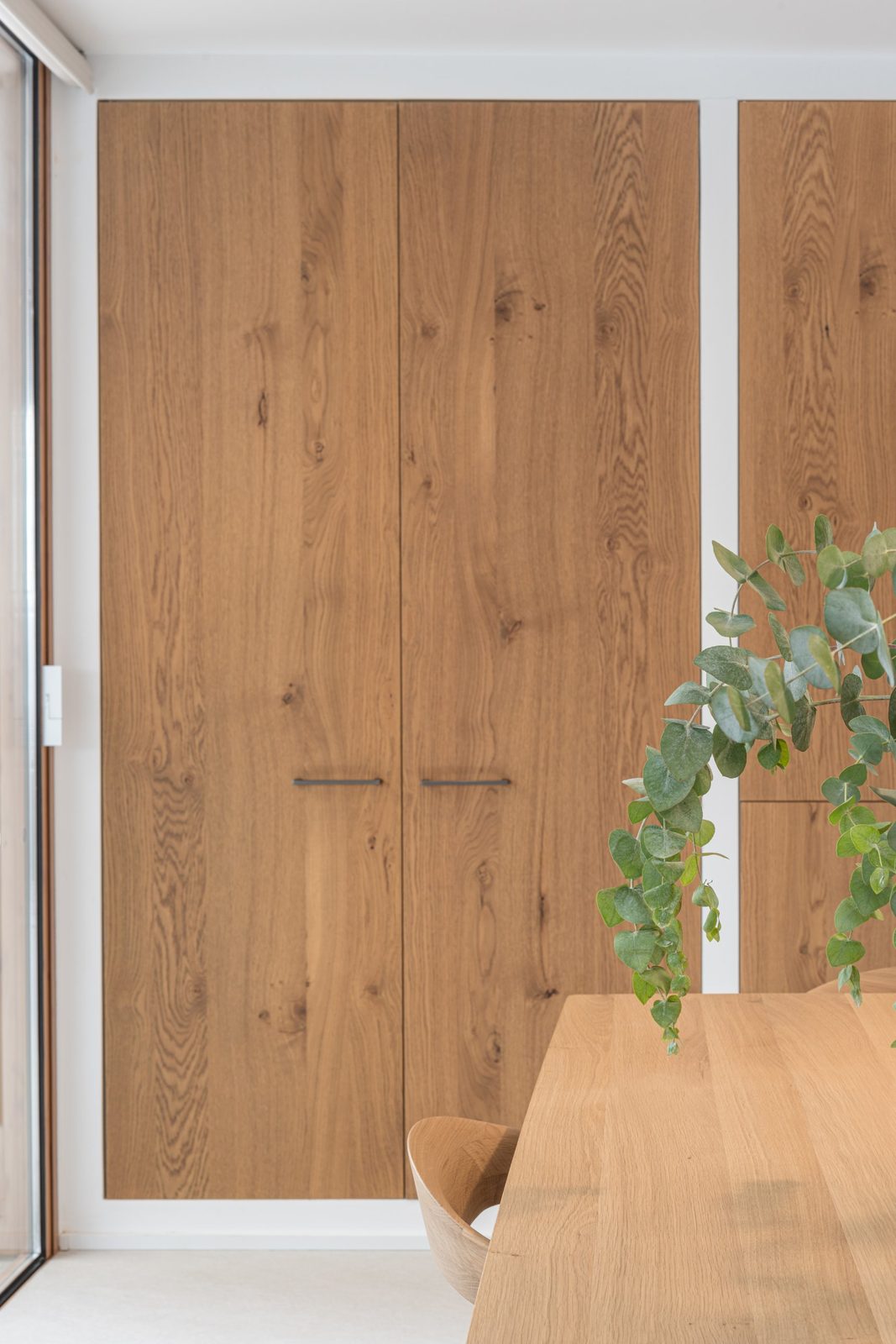 Floor-to-ceiling oak pantry doors behind an oak dining table with eucalyptus