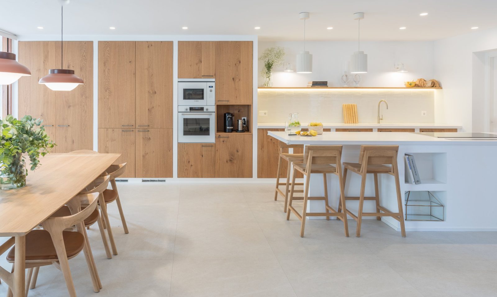 Open-plan kitchen and dining room with oak cabinetry, white island and oak furniture