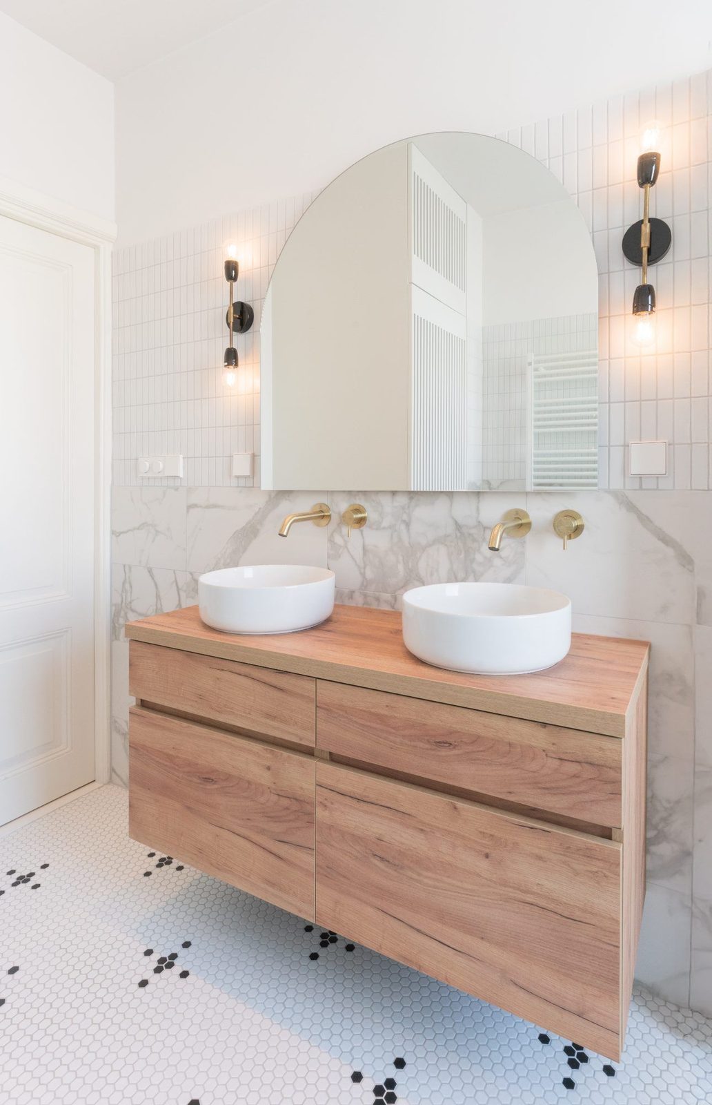 Oak bathroom vanity with double basins and an arched mirror