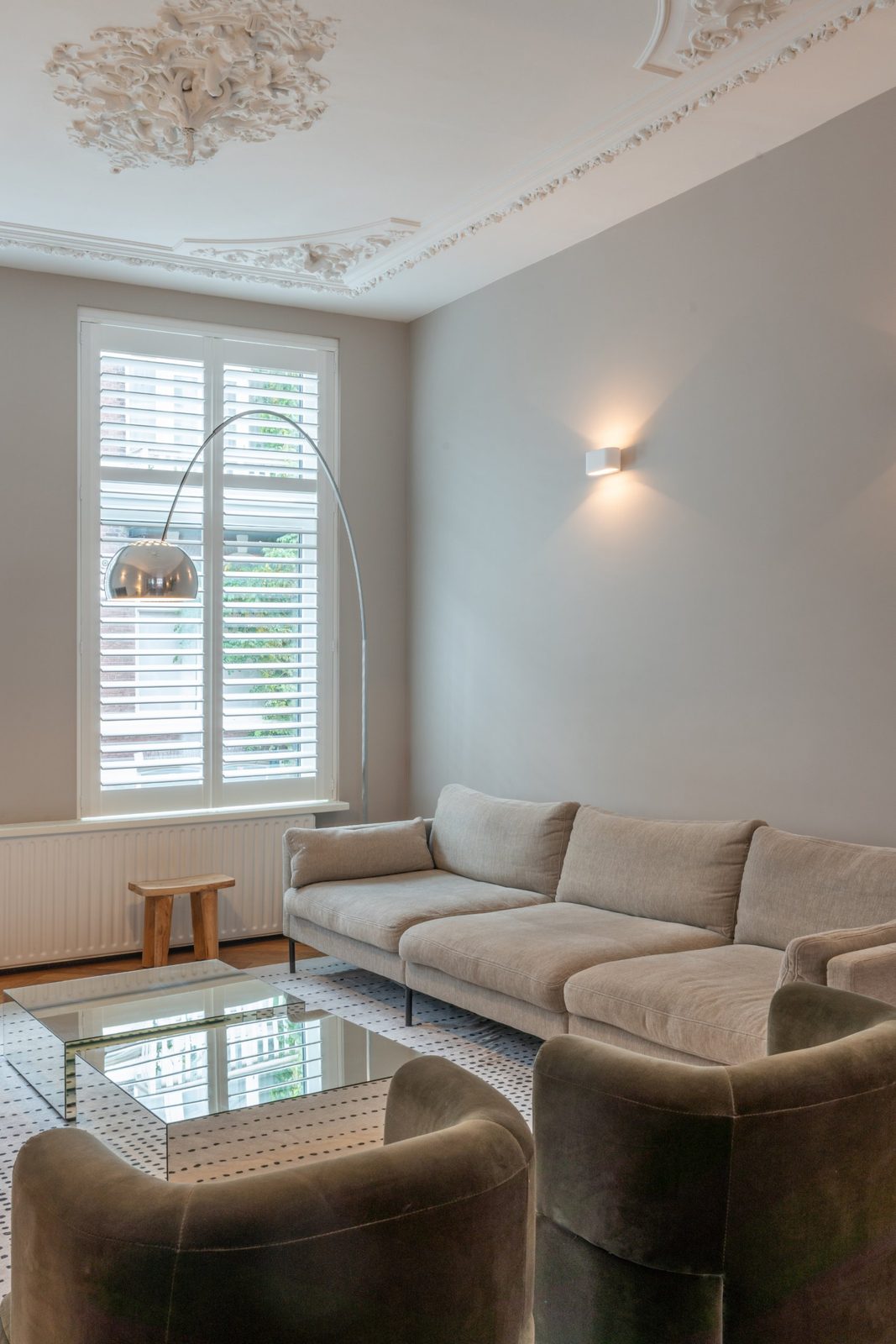 Linen sofa, arc floor lamp and plaster wall light beneath restored ceiling mouldings