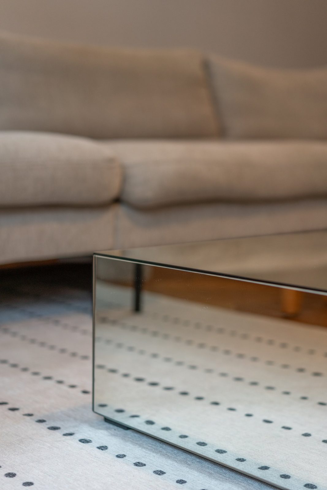 Detail of a mirrored coffee table reflecting a dotted rug and linen sofa