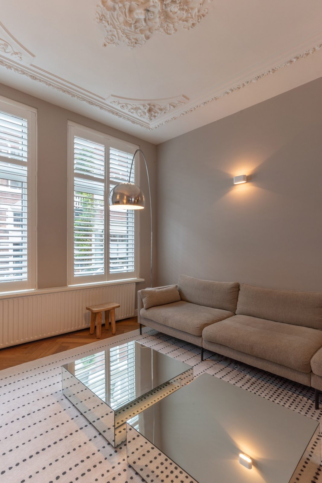 Tall windows with white plantation shutters, mirrored coffee tables and herringbone oak floor