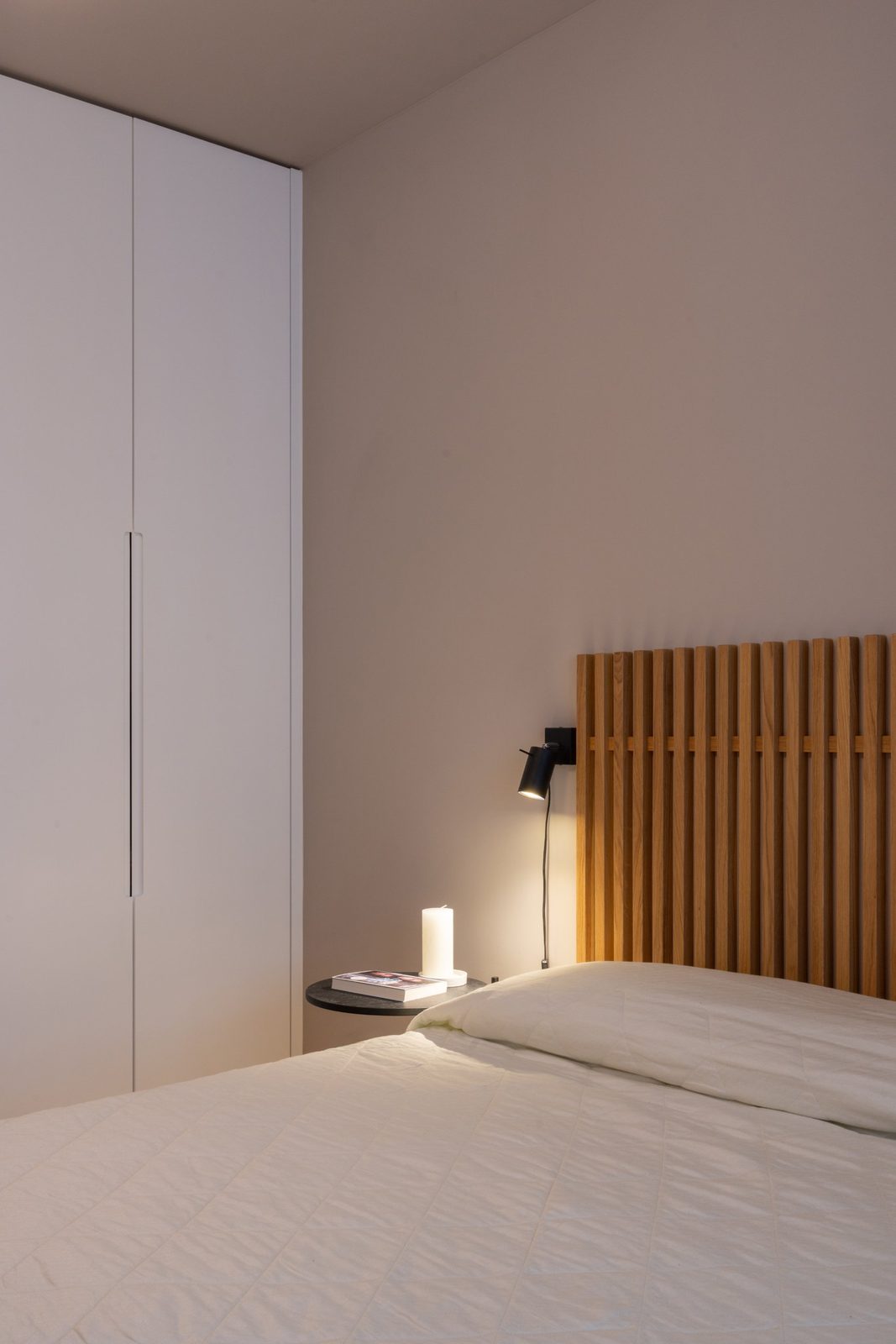 Handleless built-in wardrobe beside a slatted oak headboard and bedside reading light