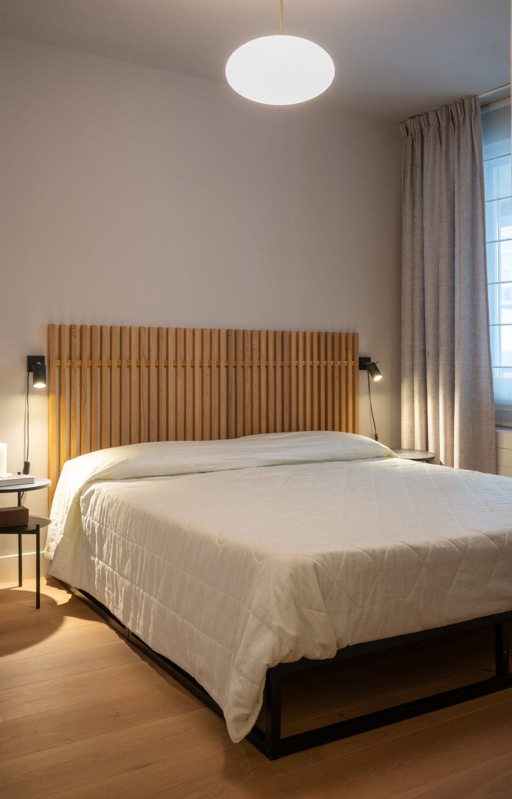 Bedroom with a slatted oak headboard, black reading lights and a glass pendant