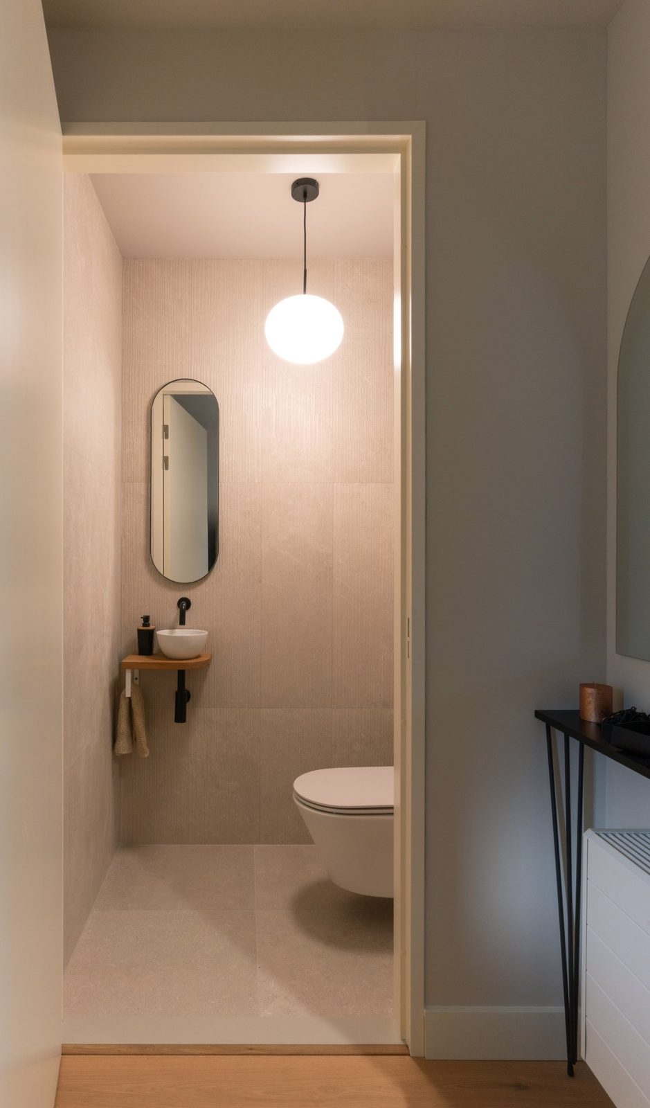 Guest toilet seen from the hall, with a globe pendant, oval mirror and small oak basin shelf