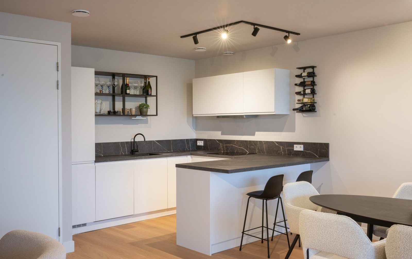 Open kitchen with white cabinets, dark veined stone worktop, black open shelving and boucle dining chairs