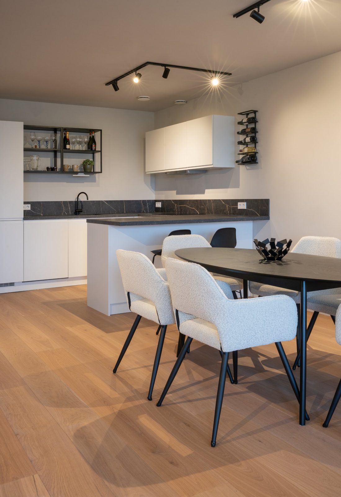 Kitchen peninsula and oval black dining table with boucle chairs on a wide oak floor