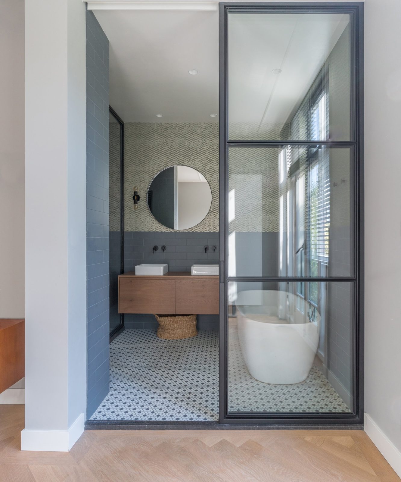 Bathroom behind a black steel-framed glass wall, with a freestanding bath and hexagonal mosaic floor