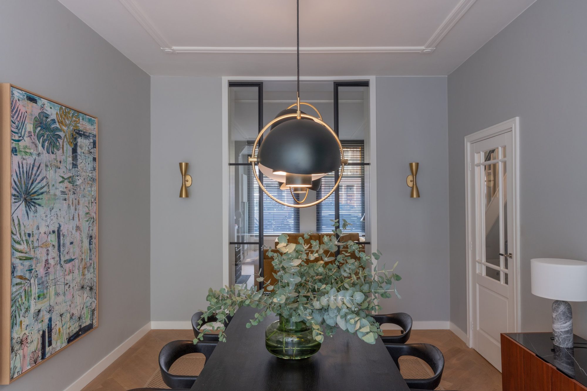 Dining room with a black oak table, brass and black pendant and steel-framed glass doors to the living room