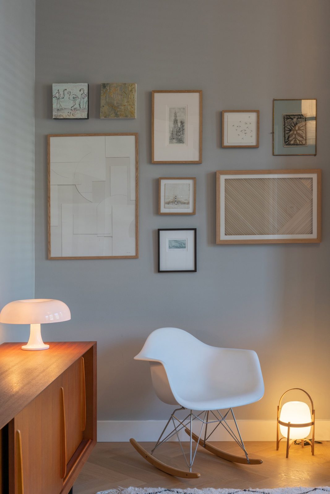 Gallery wall of framed art above a white rocking chair and a teak sideboard