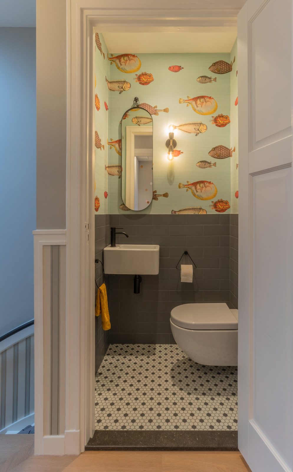 Guest toilet with bold fish wallpaper, grey tiles and an oval mirror