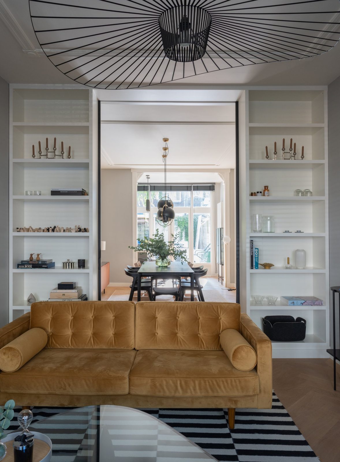 Ochre velvet sofa between built-in white shelving, with a view through to the dining room