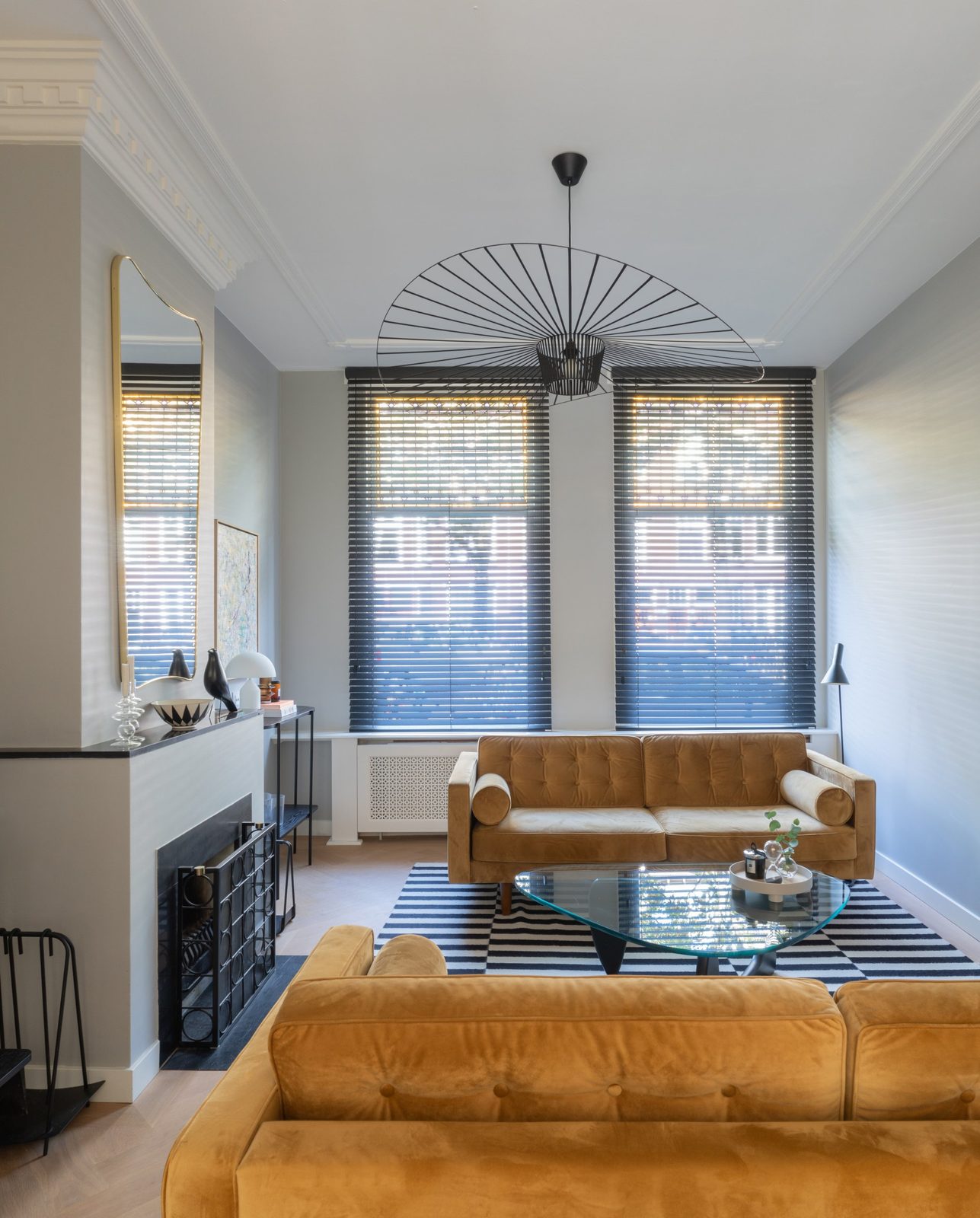 Living room with ochre velvet sofas, fireplace, brass mirror and a large wire pendant
