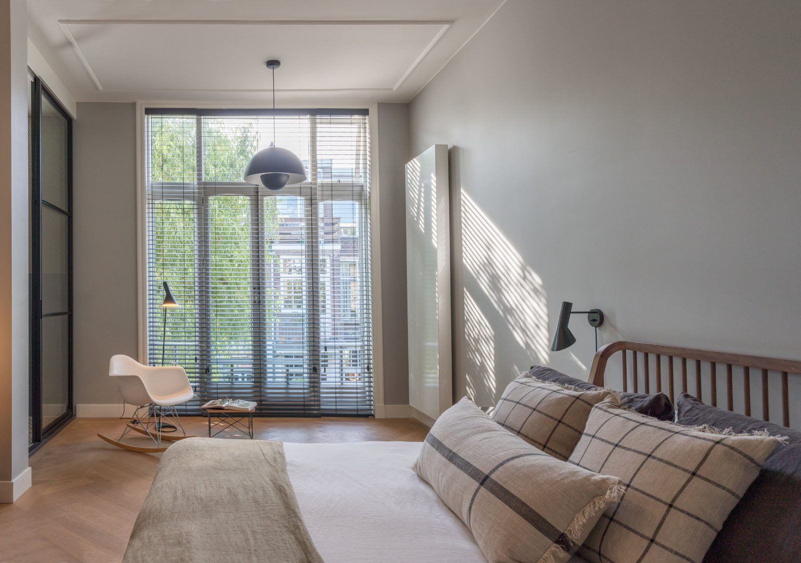 Main bedroom with tall windows, venetian blinds, rocking chair and steel-framed glass to the bathroom