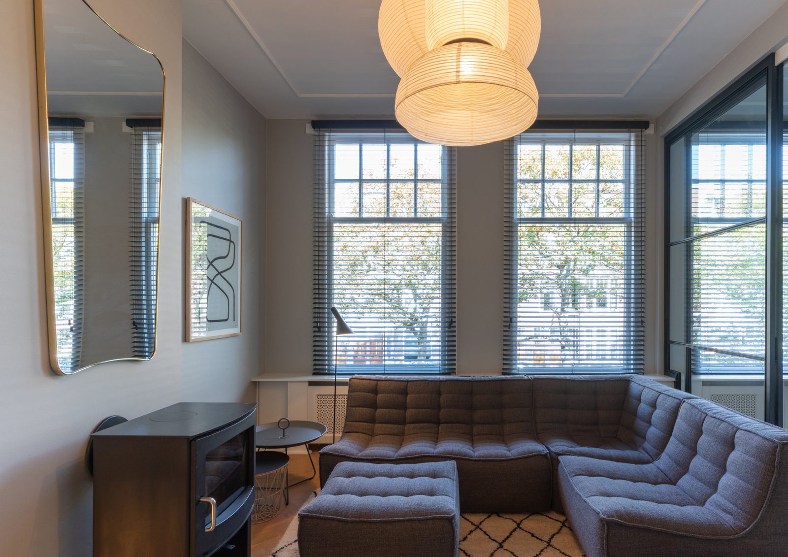 Snug with a grey modular sofa, wood stove, paper lantern and tall street-facing windows