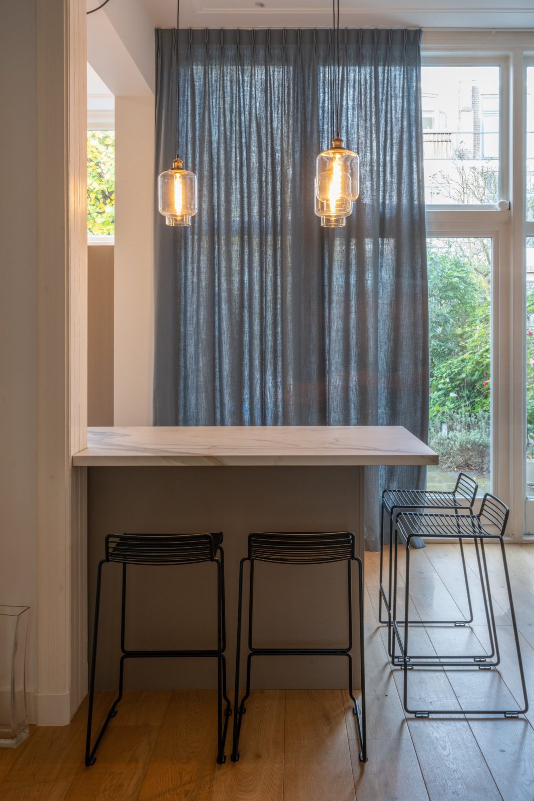 Breakfast bar with wire stools in front of a blue linen curtain and garden doors
