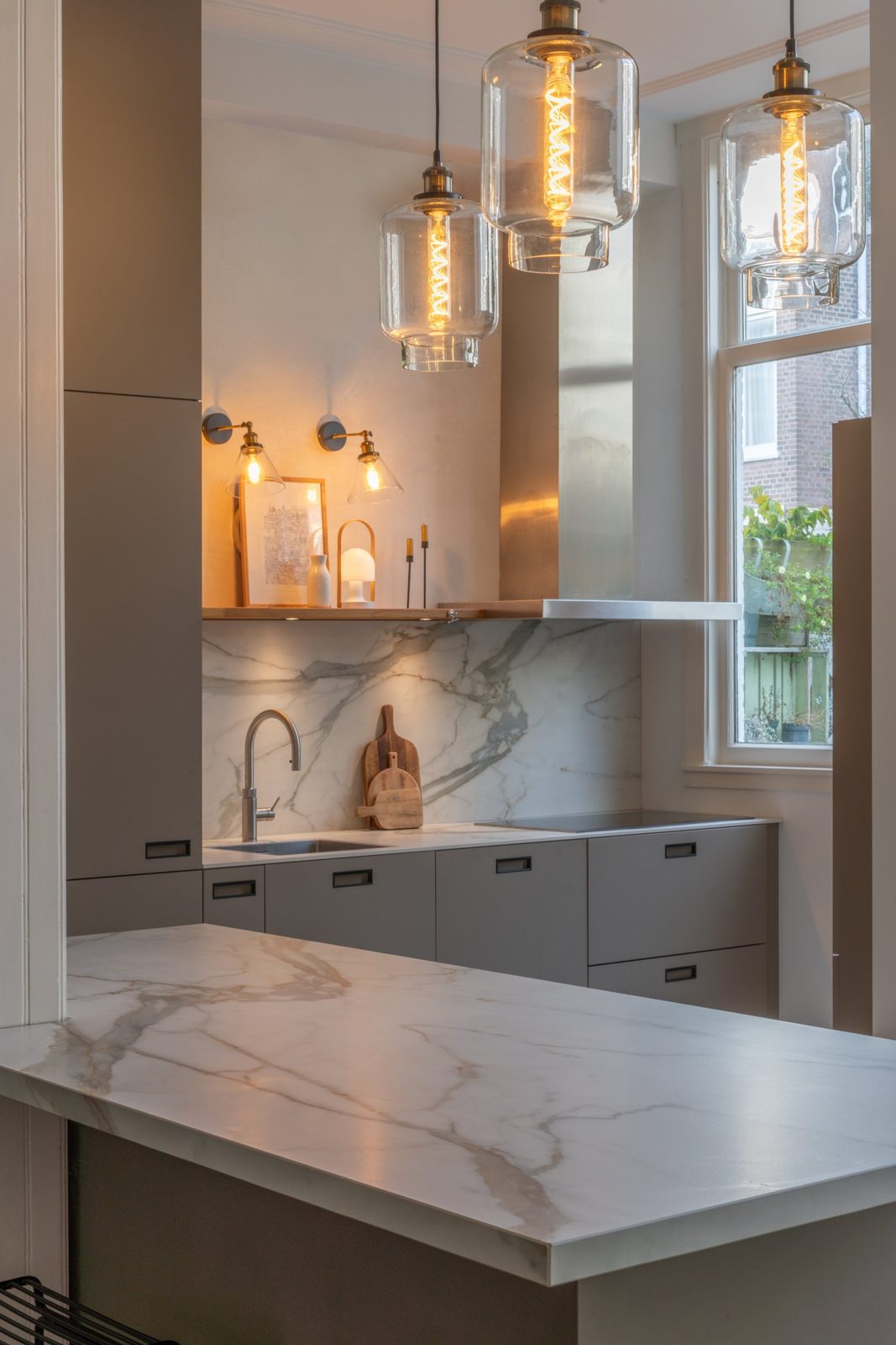 Marble splashback, oak shelf and brass wall lights under three glass pendants