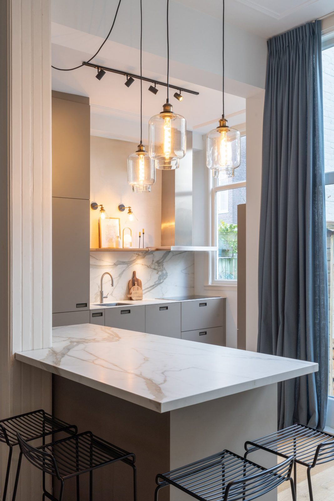 Kitchen peninsula with marble worktop, glass pendant lights and black wire bar stools