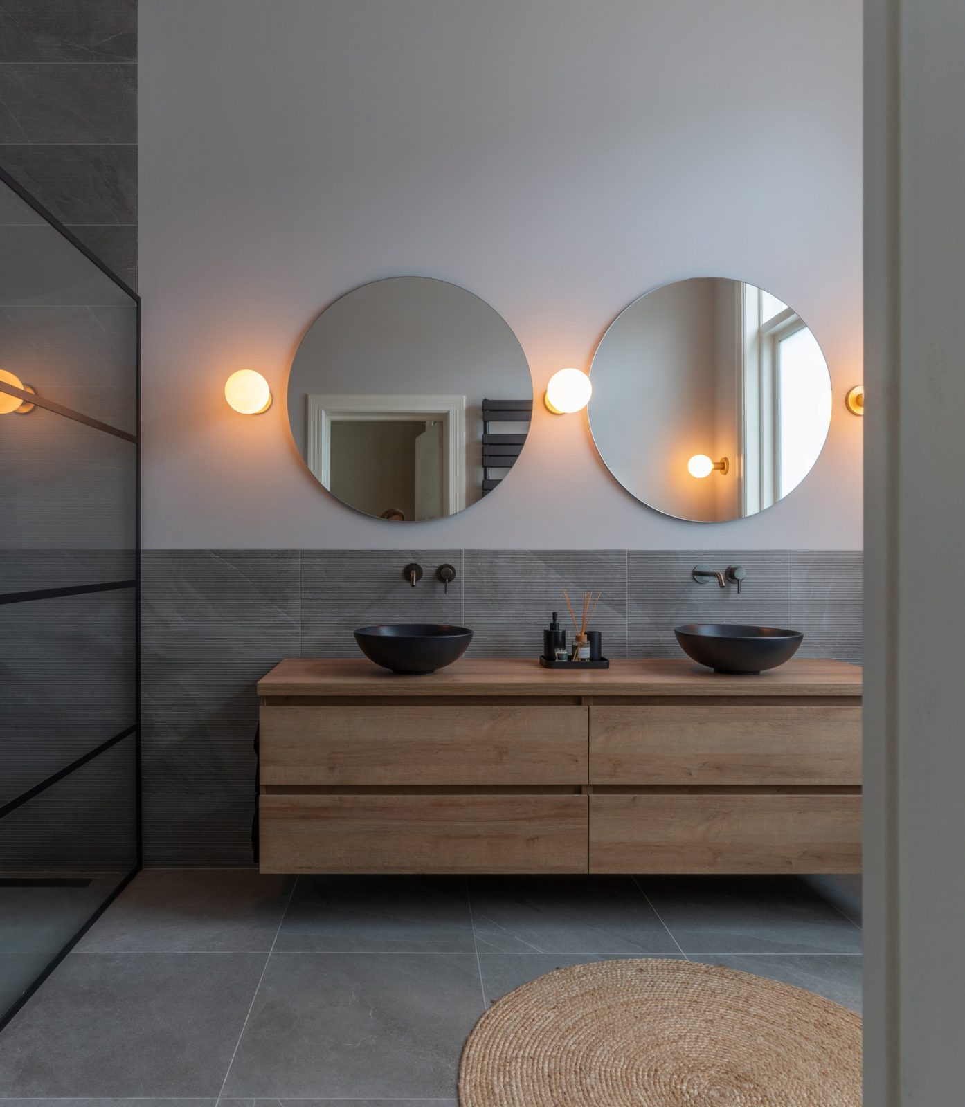 Main bathroom with a floating oak double vanity, round mirrors and brass globe lights