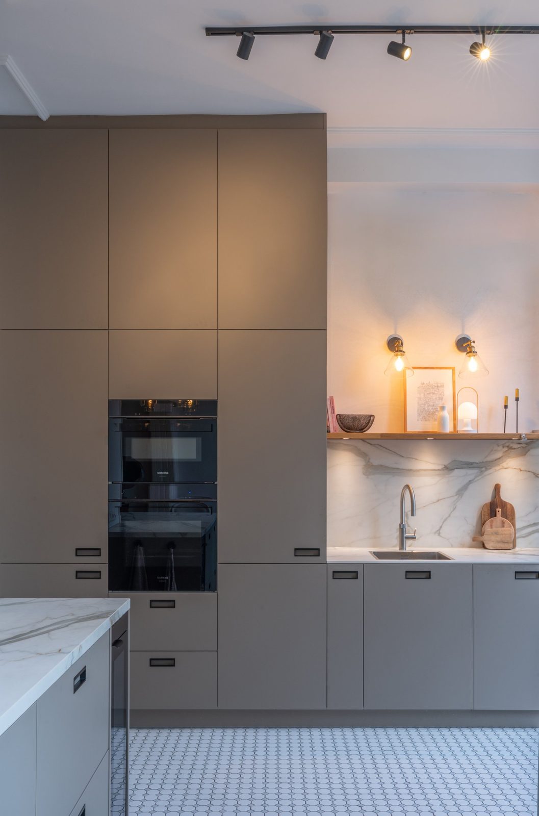 Floor-to-ceiling taupe kitchen cabinets with built-in ovens next to a marble splashback